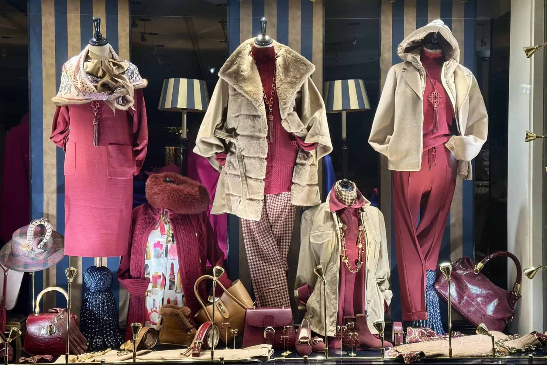 Luxe damesmode met roze en beige jassen, tassen en accessoires in een etalage voor feestdagen.