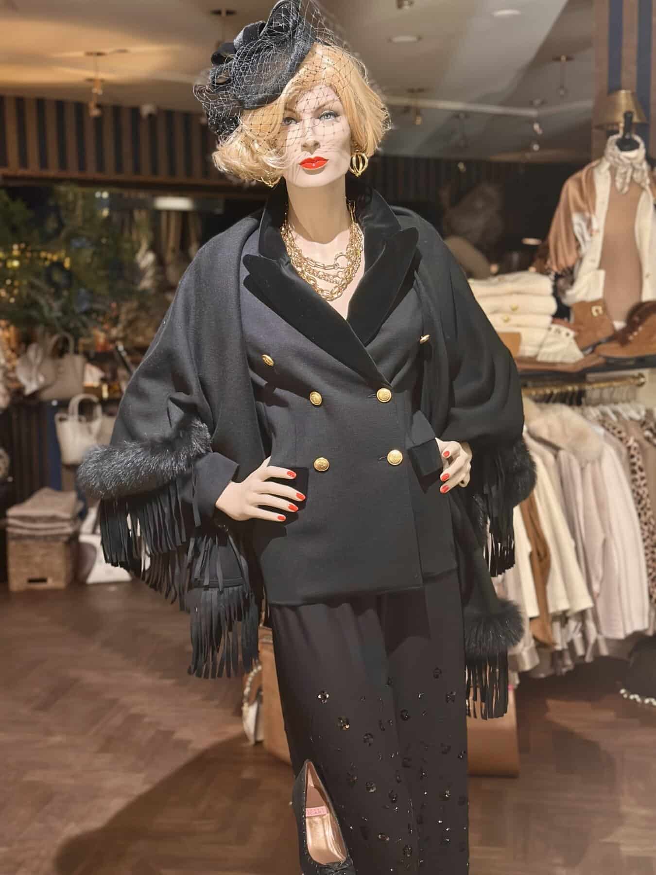 Zwarte damesoutfit met gouden knopen, fringes, en accessoires in een boetiek of winkel.