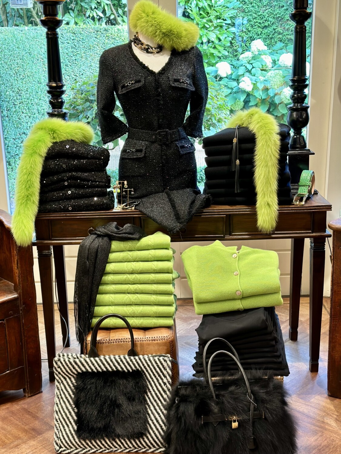 Luxueuze zwarte jurk met groene bontdetails, stijlvolle accessoires en luxe handtassen, perfect voor elegante gelegenheden.