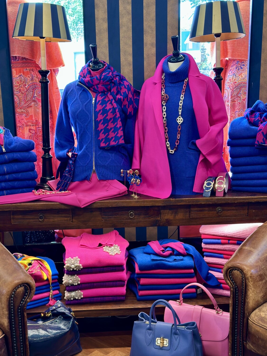 Kleding en accessoires in felle roze en blauwe tinten, stijlvolle display met truien, tassen en sieraden.
