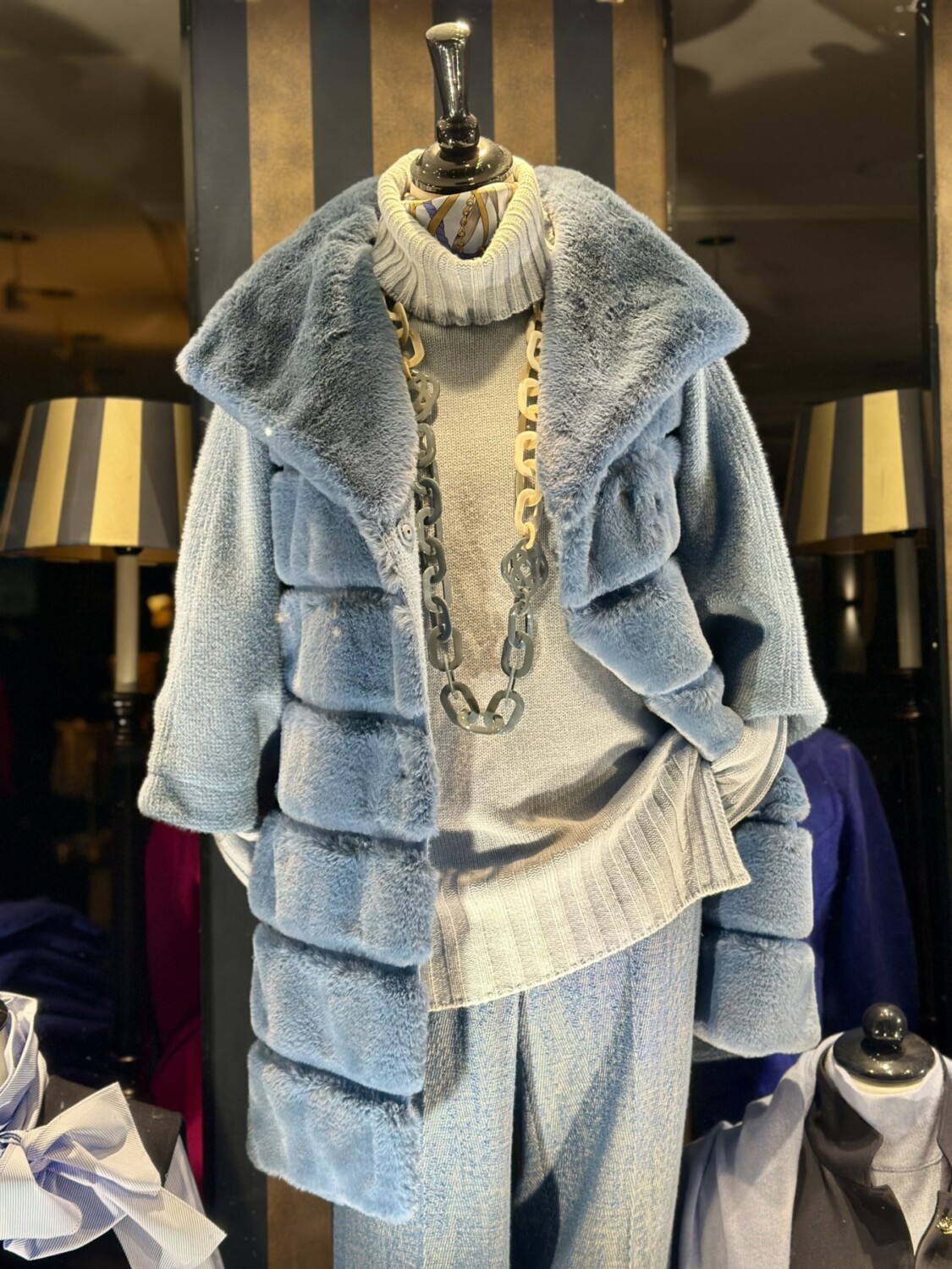 Luxe grijze winterjas en trui op mannequin met sierketting. Modici biedt stijlvolle dameskleding voor de winterperiode.