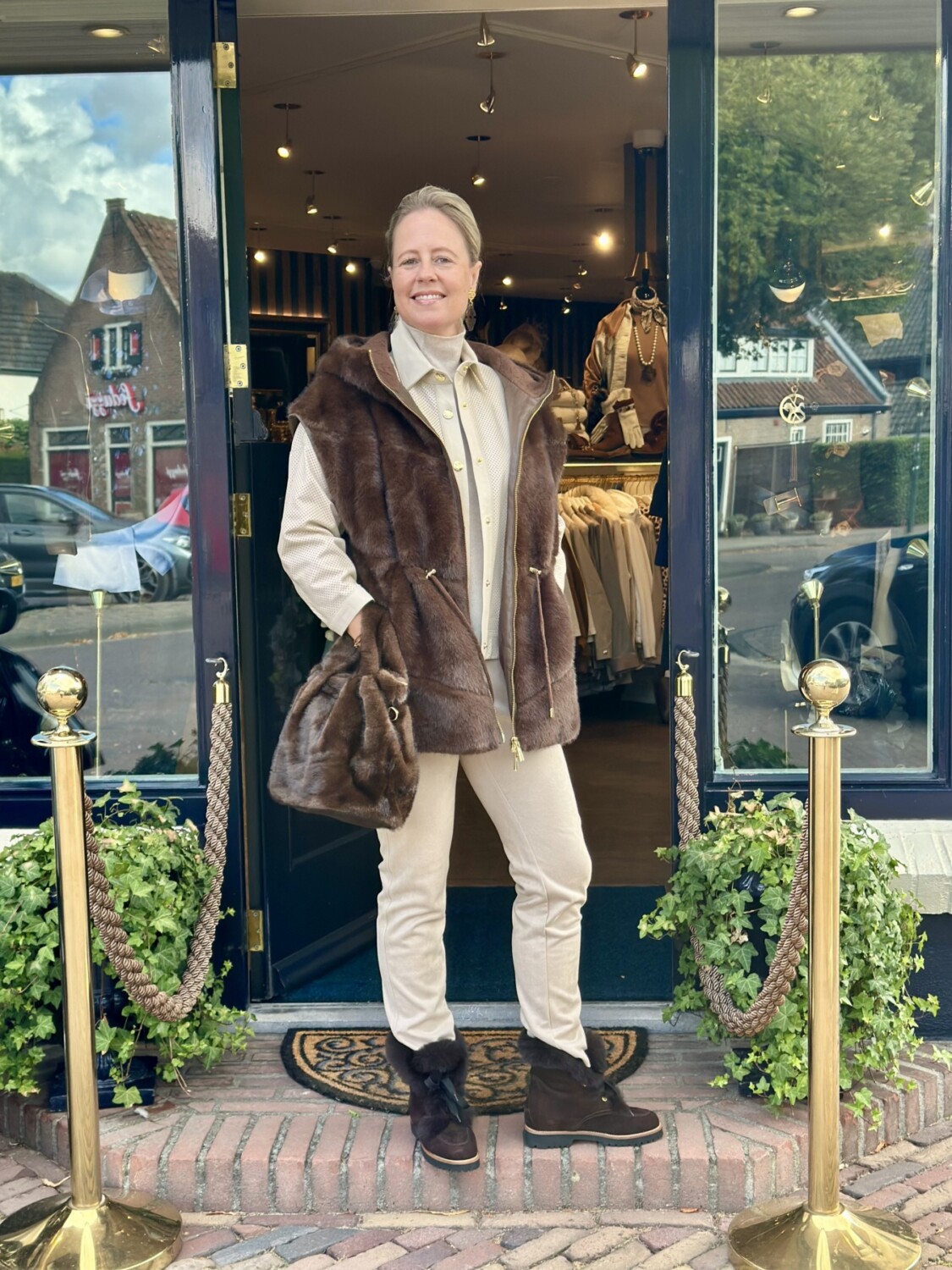 Modici, vrouw in stijlvolle winteroutfit voor winkel deur, met luxe bodywarmer jas en seductive pantalon ook in groten maten verkrijgbaar